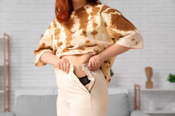 Image of woman trying to do her trousers up after pregnancy weight gain Halstead